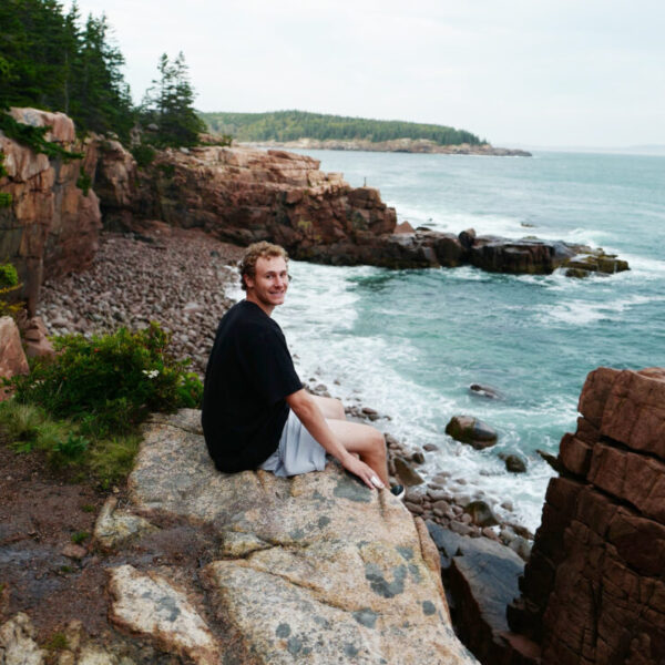 Headshot of Jonathan Barratt sitting on rocks in front of the ocean