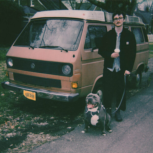 Headshot of Eli Reece with a dog in front of a vintage VW bus
