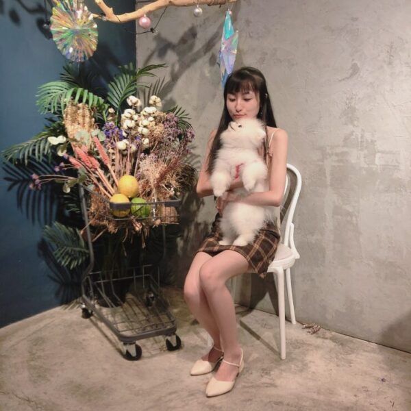 Photo of Vanessa Tu holding a white dog in front of cart with flowers and greenery