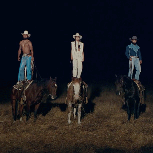 A group of Black cowboys stands on top of their horses at nighttime