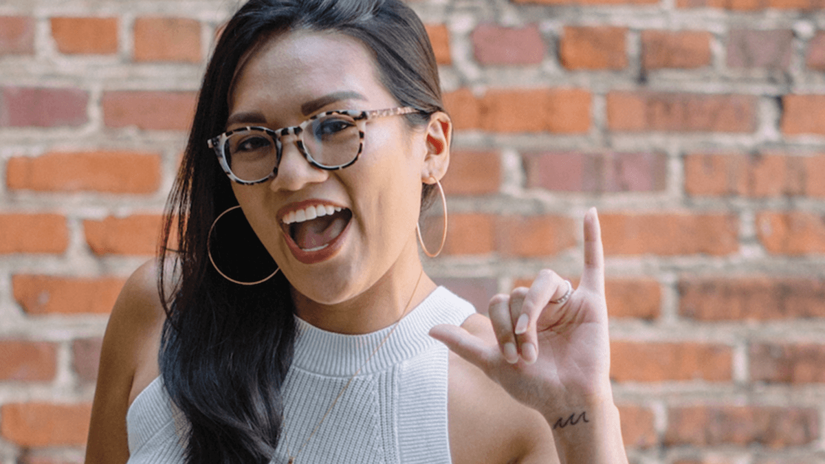 Student smiles in front of a brick wall holding up the shaka sign, the iconic hand gesture with Hawai'i origins representing “hang loose" or other friendly greetings