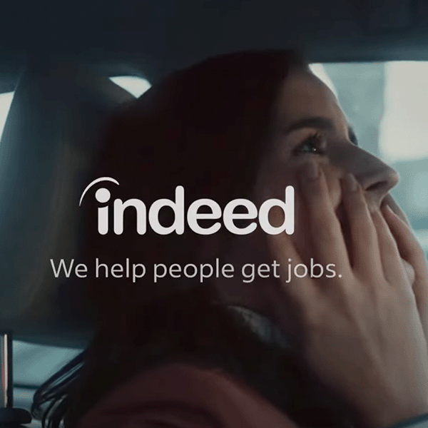 Screenshot of Indeed commercial with women sitting in car holding her face and smiling with the indeed logo and "we help people get jobs" across the screen