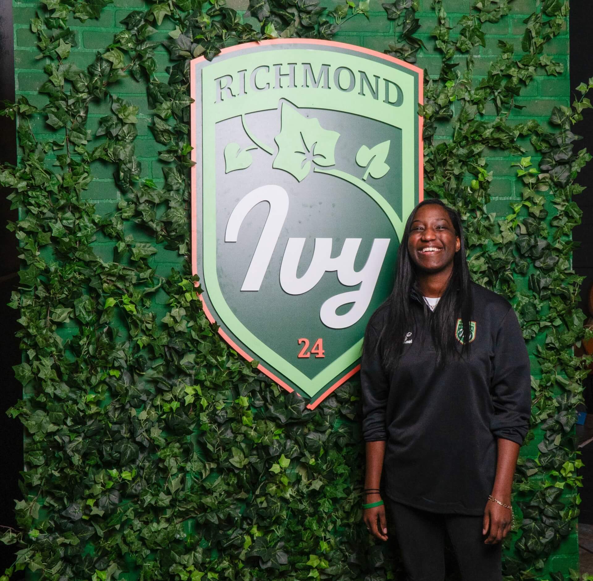 Alyn in front of a photo backdrop covered with ivy and hte richmond ivy crest