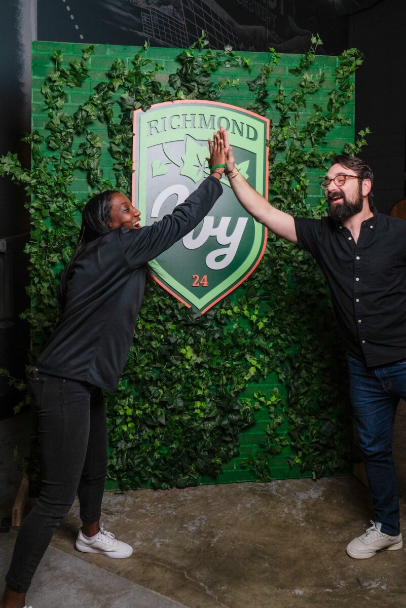 Alyn and Alex giving each other a high five in front of a photo backdrop with ivy and the richmond ivy crest