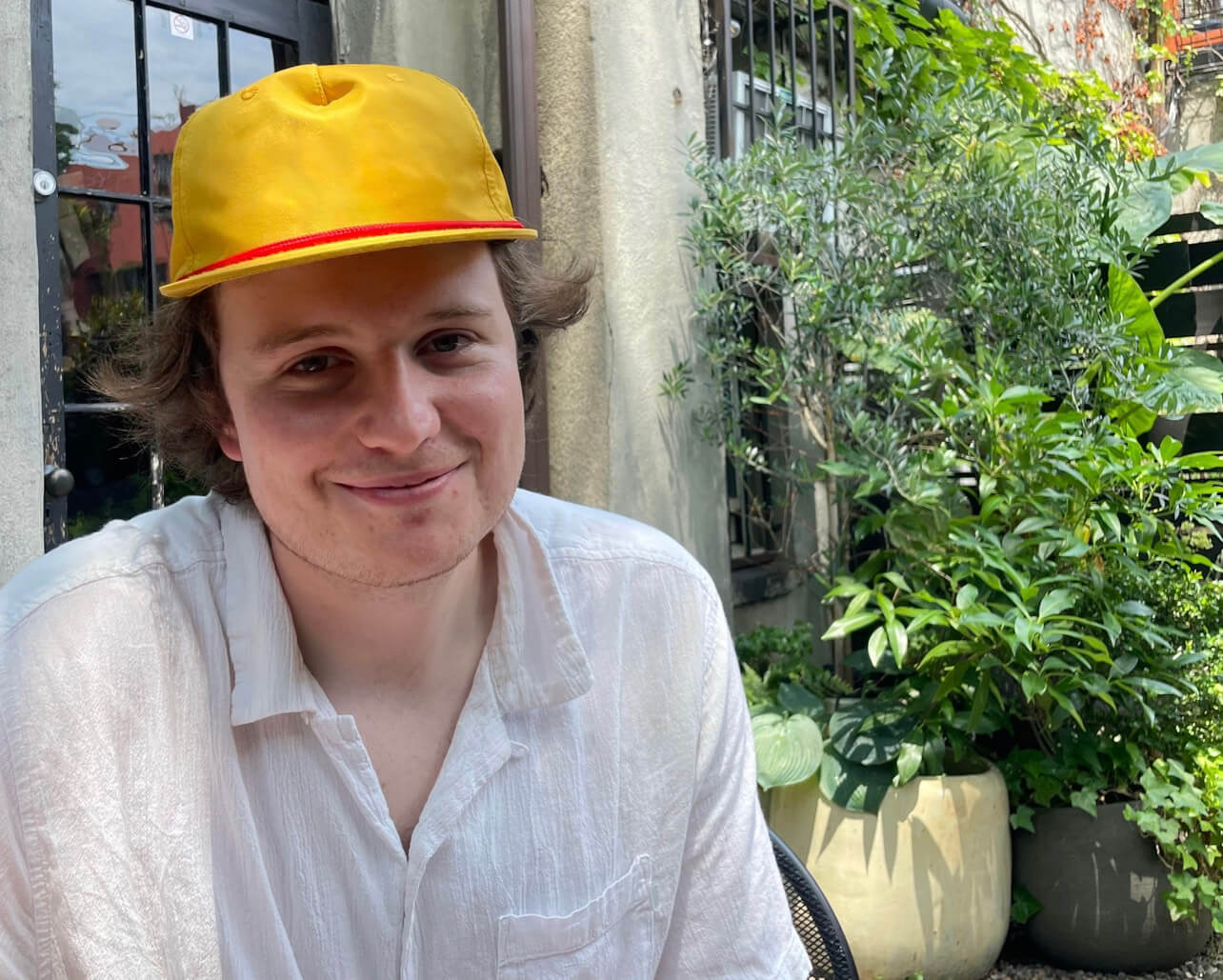 henry sitting outside in yellow hat in front of greenery